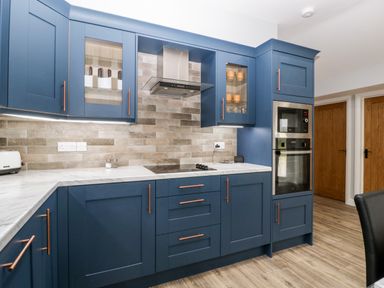 A kitchen with blue cabinets a stovetop a microwave an oven and wooden doors at Strawberry Stables in Iwood near Congresbury