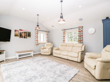 A living room with cream sofas a fluffy rug two windows with chevron curtains and a wall clock at Strawberry Stables in Iwood near Congresbury