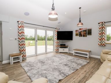 A living room with sliding glass doors a television on a stand a large rug and chevron patterned curtains at Strawberry Stables in Iwood near Congresbury