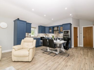 A kitchen and dining area with blue cabinets black chairs and a beige armchair at Strawberry Stables in Iwood near Congresbury