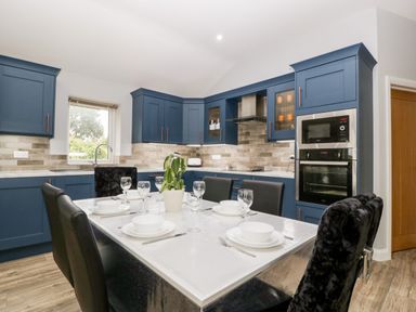 A kitchen with blue cabinets a dining table set with white dishes and glasses and black chairs at Strawberry Stables in Iwood near Congresbury