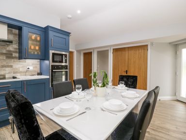 A kitchen with blue cabinets a dining table set with white dishes and glassware and black chairs at Strawberry Stables in Iwood near Congresbury