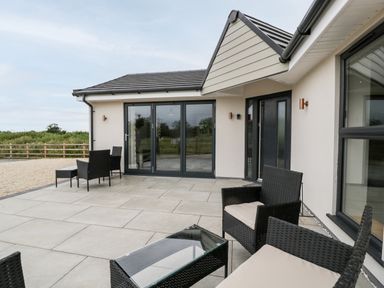 A patio with outdoor wicker chairs and a glass table outside a house at Strawberry Stables in Iwood near Congresbury