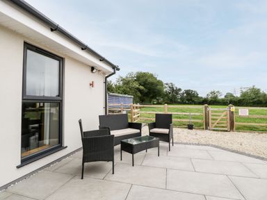 A patio area with wicker outdoor furniture and a wooden fence with gate at Strawberry Stables in Iwood near Congresbury