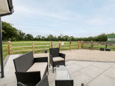 An outdoor patio with a wicker sofa set and glass table overlooking a fenced grassy field at Strawberry Stables in Iwood near Congresbury