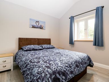 A bedroom with a double bed two bedside cabinets and a window with blue curtains at Strawberry Stables in Iwood near Congresbury