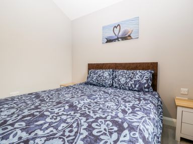 A bedroom with a bed with patterned bedding two bedside tables and a swan painting on the wall at Strawberry Stables in Iwood near Congresbury
