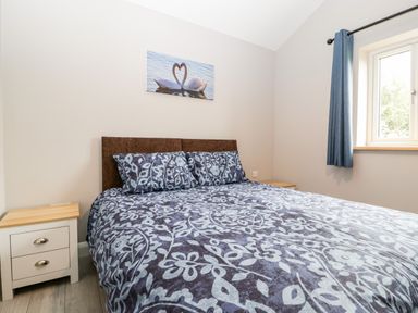 A bedroom with a bed covered in patterned bedding two bedside tables and a window with blue curtains at Strawberry Stables in Iwood near Congresbury