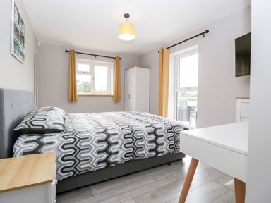 A bedroom with a bed a white wardrobe yellow curtains and a wall-mounted television at Strawberry Stables in Iwood near Congresbury