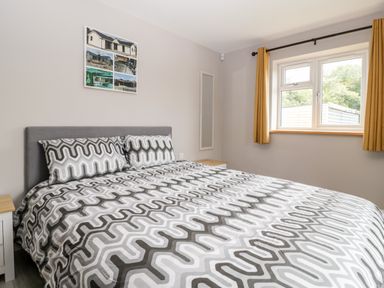 A bedroom with a bed with patterned bedding beside a window with curtains at Strawberry Stables in Iwood near Congresbury