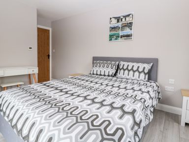 A bedroom with a bed with patterned bedding a wooden door a white desk with a stool and framed photos on the wall at Strawberry Stables in Iwood near Congresbury
