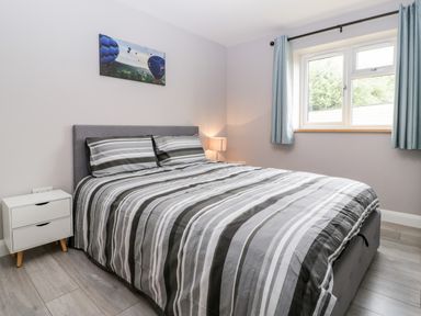 A bedroom with a double bed striped bedding bedside table with lamp window with blue curtains and a wall painting of hot air balloons at Strawberry Stables in Iwood near Congresbury