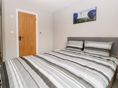 A bedroom with a double bed with striped bedding a wooden door and a painting of hot air balloons on the wall at Strawberry Stables in Iwood near Congresbury
