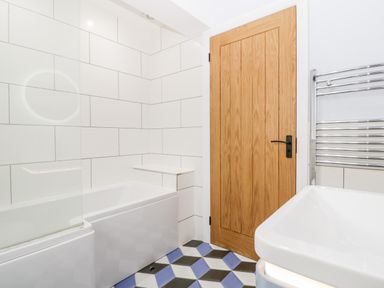 A bathroom with a bathtub a geometric tiled floor a wooden door and a white sink at Strawberry Stables in Iwood near Congresbury