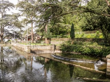 A small weir with flowing water surrounded by trees and shrubs near a stone wall in a park at Strawberry Stables in Iwood near Congresbury