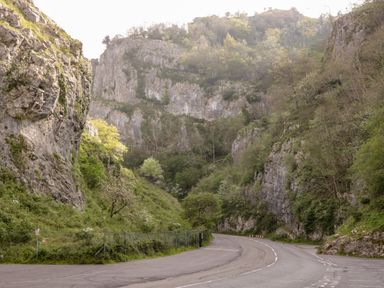 A winding road passing through a rocky valley with green trees and vegetation at Strawberry Stables in Iwood near Congresbury