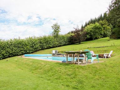 An outdoor swimming pool with plastic chairs and a table on a grassy hill surrounded by trees at Callow Fold in Dinchope near Craven Arms