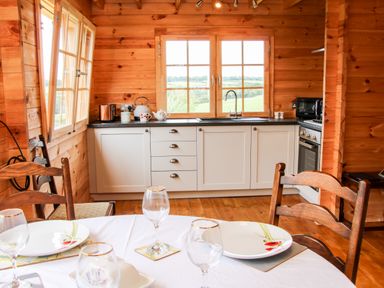 A kitchen with white cabinets wooden walls a table set with plates and glasses at Callow Fold in Dinchope near Craven Arms