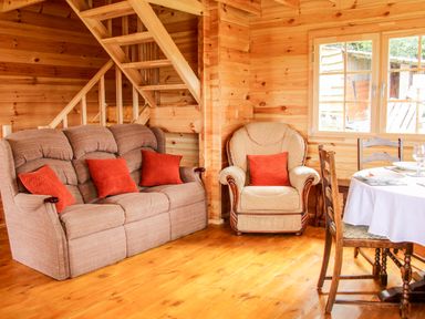 A wooden living area with a sofa and armchair with orange cushions and a dining table with chairs at Callow Fold in Dinchope near Craven Arms