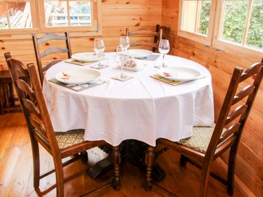 A wooden dining room with a round table covered with a white tablecloth set with plates glasses and coasters at Callow Fold in Dinchope near Craven Arms