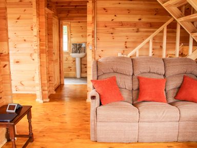 A living room with a beige sofa and orange cushions next to wooden stairs and a wooden side table with a digital device in Callow Fold in Dinchope near Craven Arms