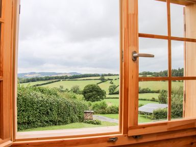 A view of green fields and trees through an open wooden window at Callow Fold in Dinchope near Craven Arms