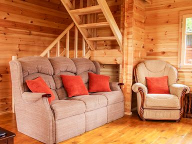 A wooden living room with a sofa and armchair with orange cushions at Callow Fold in Dinchope near Craven Arms