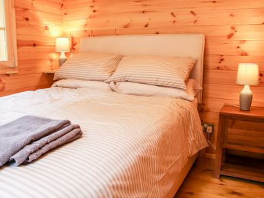 A bedroom with a double bed two bedside lamps wooden walls and folded towels at Callow Fold in Dinchope near Craven Arms
