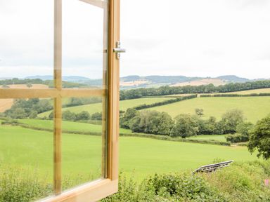 Green fields and trees seen through an open wooden window at Callow Fold in Dinchope near Craven Arms