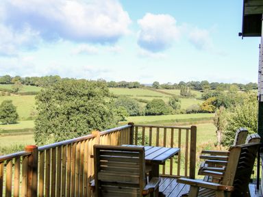 A wooden balcony with table and chairs overlooking fields and trees at Callow Fold in Dinchope near Craven Arms