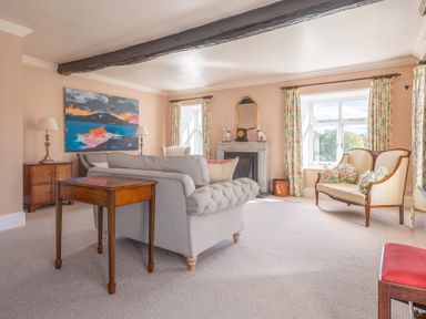 A sitting room with a grey sofa, wooden tables, a fireplace, floral curtains, and a cream settee at Field Head House in Graythwaite near Hawkshead