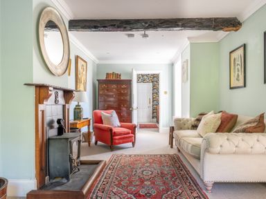 A living room with a red armchair a cream sofa a wooden fireplace and a chest of drawers at Field Head House Graythwaite near Hawkshead