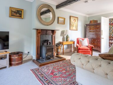 A living room with a fireplace armchair chest of drawers and a patterned rug at Field Head House in Graythwaite near Hawkshead