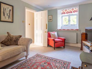 A living room with a beige sofa and red armchair near a window and a patterned rug on the floor at Field Head House in Graythwaite near Hawkshead