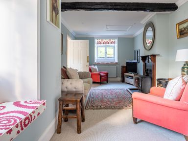 A sitting room with upholstered chairs a wooden stool a fireplace and a red patterned rug at Field Head House in Graythwaite near Hawkshead