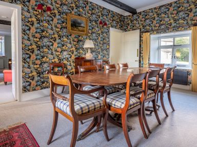A dining room with a wooden table and plaid cushioned chairs near a window at Field Head House Graythwaite near Hawkshead