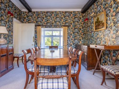 A dining room with a wooden table and chairs with plaid cushions and floral wallpaper at Field Head House in Graythwaite near Hawkshead