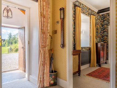 A hallway with an open wooden door leading outside a room with an umbrella stand and curtains at Field Head House in Graythwaite near Hawkshead