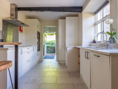 A kitchen with white cabinets a wooden stool and a window with a plant at Field Head House in Graythwaite near Hawkshead