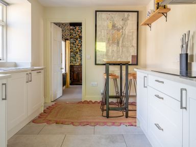 A kitchen with white cabinets a wooden table with stools and a large framed map on the wall at Field Head House Graythwaite near Hawkshead