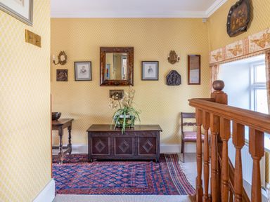 A hallway with a wooden chest and chair a patterned rug and framed pictures on yellow patterned walls at Field Head House Graythwaite near Hawkshead