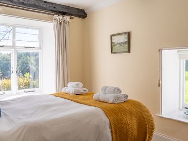 A bedroom with a bed covered in white sheets and a yellow blanket with rolled towels on top at Field Head House in Graythwaite near Hawkshead