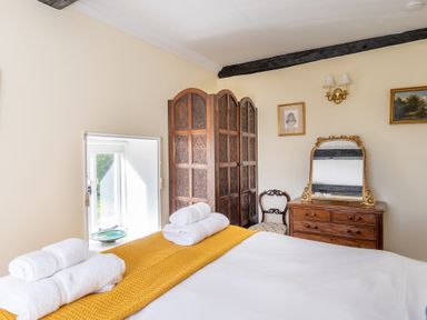 A bedroom with a bed with towels on it a wooden screen chair and dresser with mirror at Field Head House in Graythwaite near Hawkshead