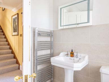 A bathroom with a pedestal sink and a towel radiator next to a staircase with carpet and framed artwork at Field Head House in Graythwaite near Hawkshead