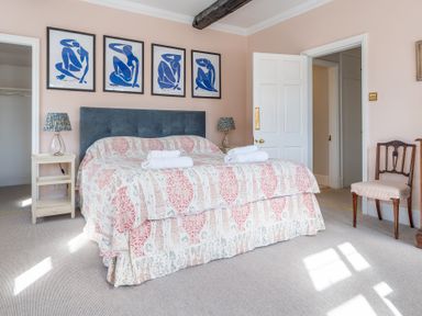 A bedroom with a double bed and blue headboard two bedside tables with lamps and framed art on wall at Field Head House Graythwaite near Hawkshead