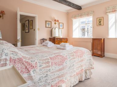 A bedroom with a bed covered in patterned bedding two windows and wooden furniture at Field Head House Graythwaite near Hawkshead