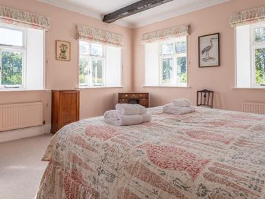 A bedroom with a patterned bedspread and folded towels on the bed with three windows and wooden furniture at Field Head House Graythwaite near Hawkshead