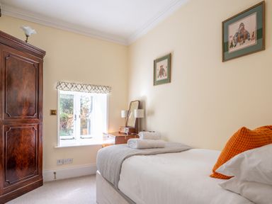 A bedroom with a single bed orange pillow wooden dresser and wardrobe at Field Head House Graythwaite near Hawkshead