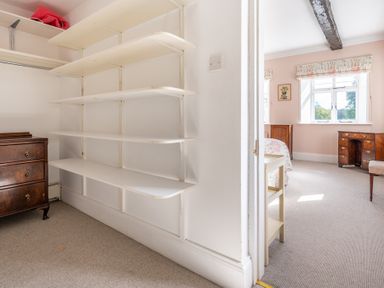 A room with white shelves and a wooden chest of drawers leading to a bedroom with wooden furniture and windows at Field Head House in Graythwaite near Hawkshead
