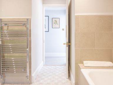 A bathroom with a towel radiator bathtub and an open door showing artwork in the next room at Field Head House in Graythwaite near Hawkshead